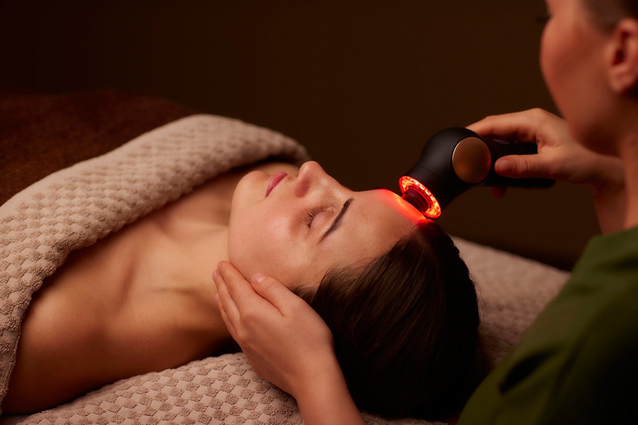 Spa therapist giving a woman a Theraface microcurrent facial treatment.